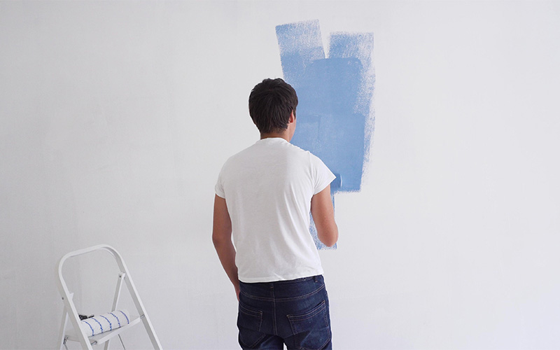 Man using a roller to apply blue paint to a wall.