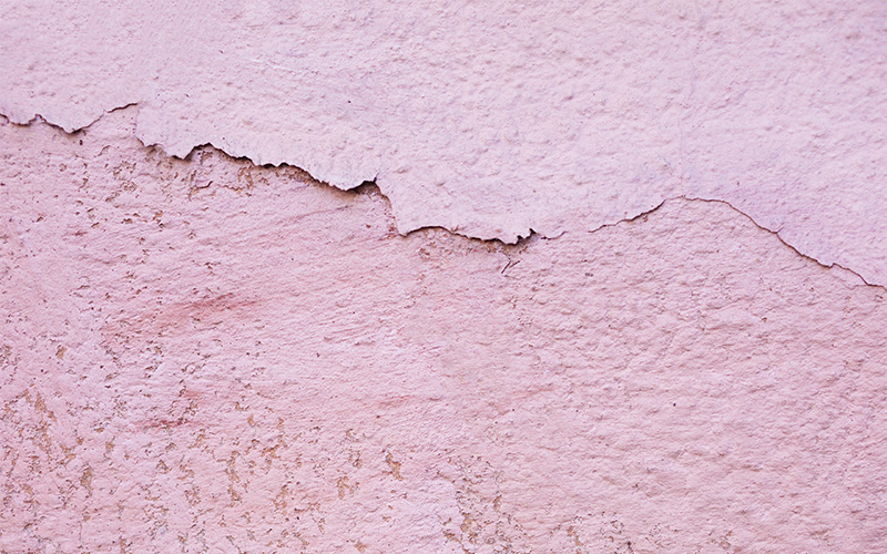 Close-up of cracked and peeling pink wall plaster finish.